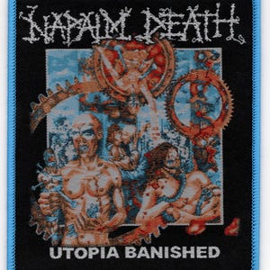May include: Black patch with a blue border featuring the band name "NAPALM DEATH" in white, stylized lettering. The patch has a graphic illustration in shades of orange, blue, and brown, with the words "UTOPIA BANISHED" in white at the bottom.