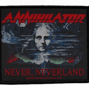 May include: A square black fabric patch featuring the red text ANNIHILATOR at the top and NEVER, NEVERLAND at the bottom. The center displays a woven graphic of a face surrounded by dark clouds and the text 2008 NEVERLAND MUSIC INC.