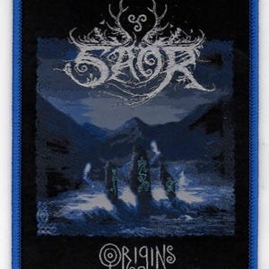 May include: Black and blue embroidered patch with the band name "SAOR" in a stylized font and the words "ORIGINS" below. The patch features a mountain range and figures in the background.