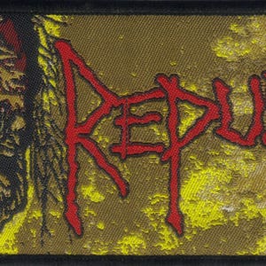 May include: A rectangular fabric patch featuring a graphic illustration of a decaying zombie head on the left side and the word REPULSION written in a jagged, red, stylized font on the right, set against a distressed yellow and brown background.