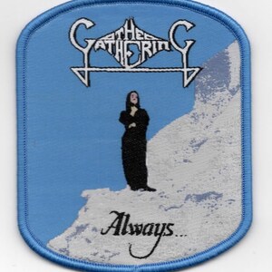 May include: A light blue patch with a blue border featuring the band name "Gathering" in white gothic lettering. The patch depicts a person in black standing on a snowy cliff, with the word "Always..." below.