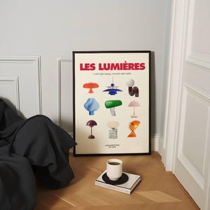May include: A framed poster titled "LES LUMI&Egrave;RES" with various colorful lamp designs. The poster is on a light-colored wall, and a white coffee cup sits on a book on the floor. The text "I call it light design, my bank calls it debt" is also on the poster.
