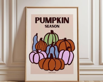 Op de afbeelding: Een ingelijste kunstprint met een verzameling gestileerde pompoenen in verschillende kleuren, waaronder oranje, groen, blauw en roze. De woorden "PUMPKIN SEASON" staan bovenaan gedrukt. De print heeft een beige achtergrond en is ingelijst in goud.