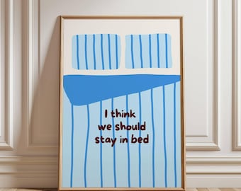 Op de afbeelding: Een ingelijste print met een bed met blauw gestreepte beddengoed en kussens. De rode tekst luidt "I think we should stay in bed". Het kunstwerk wordt getoond tegen een witte muur.