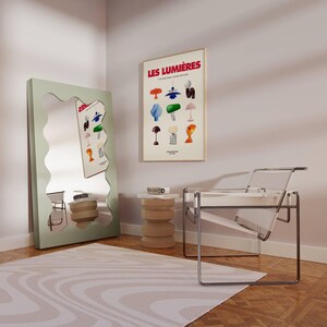 May include: A room interior featuring a large, wavy-edged, mint-green mirror and a framed poster with the text "LES LUMI&Egrave;RES". A clear chair and a beige side table are also visible. The room has a wooden floor and a patterned rug.