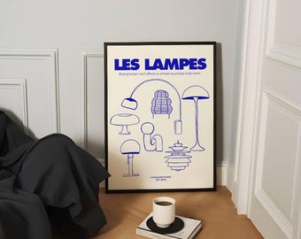 Op de afbeelding: Een ingelijste kunstdruk met blauwe lijntekeningen van lampen op een gebroken witte achtergrond. De tekst "LES LAMPES" staat bovenaan, met daaronder de zin "Buying lamps I can't afford, so at least my anxiety looks iconic". Een witte mok staat op een boek.