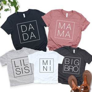 May include: Five short-sleeved t-shirts in various colors, each with a different text design inside a square. The shirts are navy blue, mauve, gray, white, and charcoal. The text on the shirts reads "DADA", "MAMA", "LIL SIS", "MINI", and "BIG BRO".