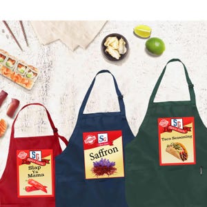 May include: Three aprons with the "Spice Girls" logo. One red apron with "Slap Ya Mama" text and chili pepper graphic. A navy blue apron with "Saffron" text and saffron graphic. A green apron with "Taco Seasoning" text and taco graphic.