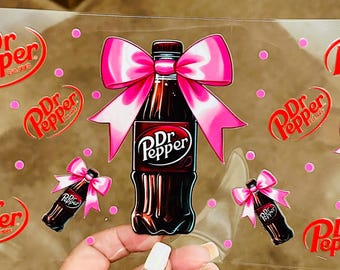 May include: A sheet of clear vinyl with multiple Dr Pepper logos and images of Dr Pepper bottles with pink bows. The bottles are brown and the bows are pink with white polka dots.