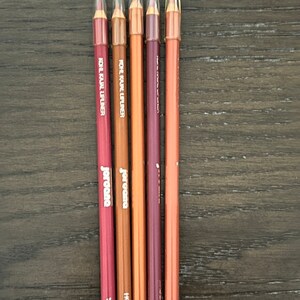 Op de afbeelding: Vijf liplinerpotloden met doorzichtige doppen. De potloden zijn gelabeld met "KOHL KAJAL LIPLINER" en "JERCOSA". De kleuren zijn rood, bruin, oranje, paars en roze.