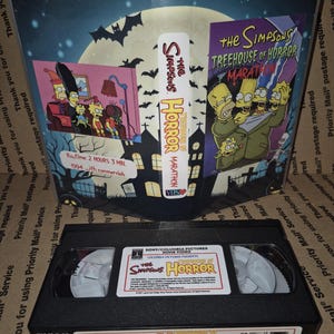 Può includere: Una videocassetta VHS nera di "The Simpsons Treehouse of Horror Marathon" con il logo dello show e l'artwork degli episodi. La copertina presenta la famiglia Simpson in un'ambientazione spettrale. Il nastro è etichettato "FUJI T-60".