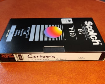 May include: A black Scotch T-120 VHS videocassette tape labeled "Cartoons with commercials" from 1986. The tape has a colorful circular design and the text "EVERYDAY USE for general purpose recording".