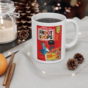 May include: White ceramic mug featuring a Kellogg's Froot Loops cereal box design. The mug displays the Froot Loops logo, a toucan mascot, and colorful cereal pieces. The mug is filled with a dark liquid.