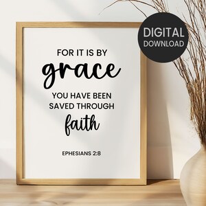May include: A framed print with the text "FOR IT IS BY grace YOU HAVE BEEN SAVED THROUGH faith EPHESIANS 2:8". The print is in a light wood frame and has a white background with black text. A black circle with "DIGITAL DOWNLOAD" is in the upper right corner.