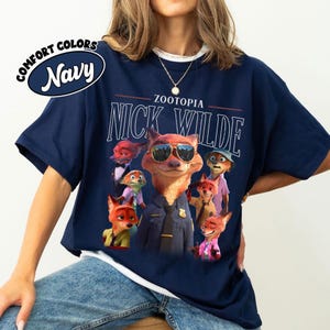 Puede incluir: Camiseta azul marino con un gr&aacute;fico de Nick Wilde de Zootopia con gafas de sol, rodeado de otros personajes. El texto "ZOOTOPIA" y "NICK WILDE" est&aacute; impreso encima de la imagen. La camiseta tiene cuello redondo y mangas cortas.