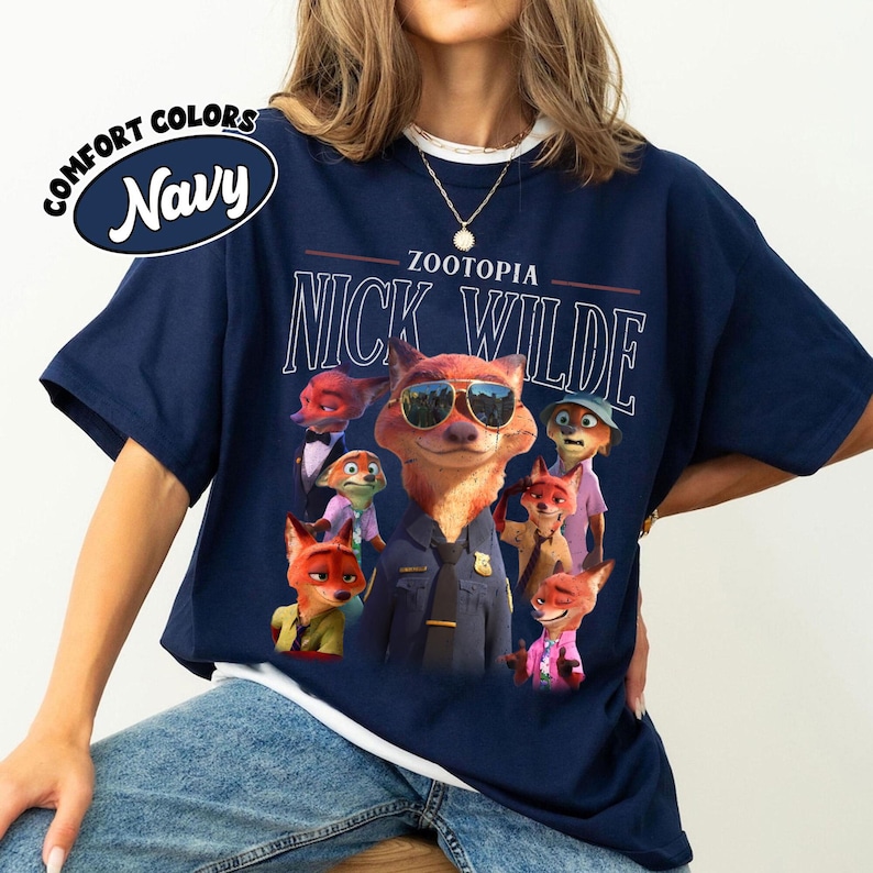 Puede incluir: Camiseta azul marino con un gr&aacute;fico de Nick Wilde de Zootopia con gafas de sol, rodeado de otros personajes. El texto "ZOOTOPIA" y "NICK WILDE" est&aacute; impreso encima de la imagen. La camiseta tiene cuello redondo y mangas cortas.