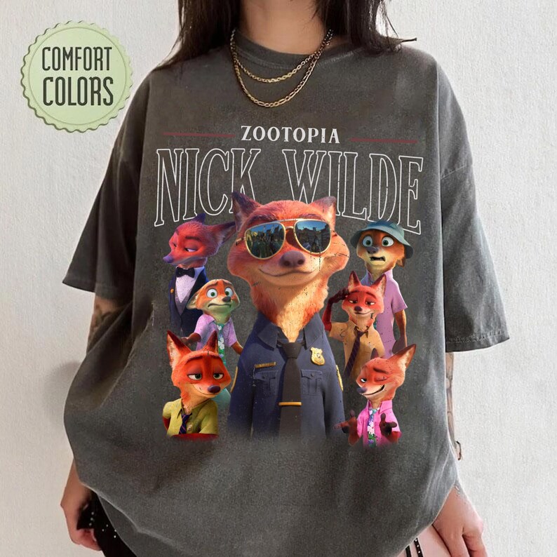 Puede incluir: Camiseta gris oscuro con un gr&aacute;fico de Nick Wilde de Zootopia con gafas de sol, rodeado de otros personajes. Los textos "ZOOTOPIA" y "NICK WILDE" est&aacute;n impresos encima del gr&aacute;fico. La camiseta tiene un logotipo de "COMFORT COLORS".