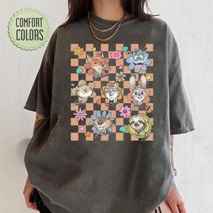 Puede incluir: Camiseta gris oscuro con personajes de dibujos animados de Zootopia sobre un fondo a cuadros con flores y corazones. La camiseta tiene el texto "Comfort Colors" en un dise&ntilde;o circular.