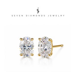 Pode incluir: Um par de brincos de tarracha com pedras transparentes de corte oval montadas em garras de ouro amarelo. O texto SEVEN DIAMONDS JEWELRY é exibido acima dos brincos, acompanhado por um logótipo com as letras S e D e um diamante.