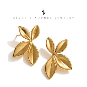 Könnte beinhalten: Ein Paar goldfarbene Ohrringe in Blattform. Jeder Ohrring hat drei gebogene, blütenblattartige Formen. Die Ohrringe sind vor einem weißen Hintergrund platziert. Der Text "SEVEN DIAMONDS JEWELRY" steht oben.
