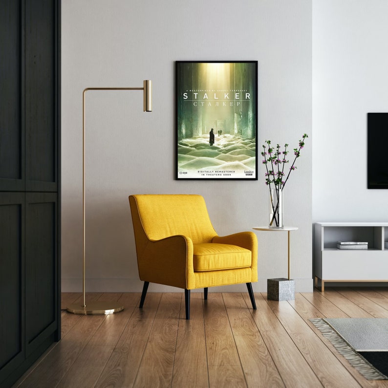 May include: A yellow armchair with black legs sits in a living room with a poster for the film "Stalker" on the wall. The poster features a man walking through a field of white sand.