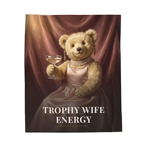 Può includere: Un orsacchiotto beige che indossa un vestito rosa, una collana di perle e orecchini dorati, mentre tiene in mano un calice di champagne. L'immagine presenta uno sfondo drappeggiato rosso scuro e il testo TROPHY WIFE ENERGY e REALITY & REVELRY.
