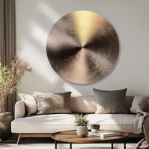 Op de afbeelding: Een groot rond wandkunstobject met een geborstelde metalen afwerking en een radiale textuur. Het oppervlak vertoont een verloop van brons- en goudtinten, die het licht vanuit het midden in een cirkelvormig patroon over de schijf reflecteren.