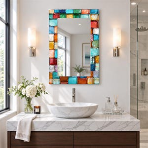 May include: A rectangular wall mirror featuring a decorative frame composed of multi-colored, translucent glass tiles in shades of blue, red, orange, yellow, and green. The glass tiles have a smooth, glossy finish and are arranged in a mosaic pattern.
