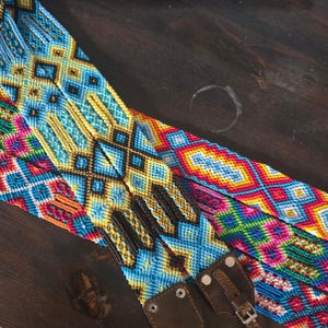 Puede incluir: Primer plano de tres cinturones tejidos coloridos con patrones geométricos. Los cinturones presentan azul, amarillo, rojo y marrón. Cada cinturón tiene una hebilla y una correa de cuero.