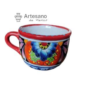 Può includere: Una tazza in ceramica dipinta a mano con un vivace motivo floreale. La tazza presenta un bordo e un manico rossi, con un colorato motivo di fiori blu, arancioni e gialli. Il testo "Artesano de Mexico" è visibile.