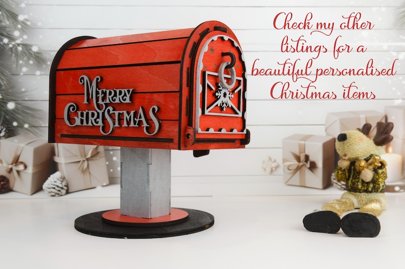 May include: A red wooden mailbox with the words "Merry Christmas" in silver lettering. The mailbox has a decorative design and sits on a gray post and black base. A reindeer figurine is to the right.