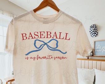 May include: A beige t-shirt with a red and blue graphic that says "Baseball is my favorite season". The graphic features a blue bow.