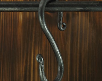 Ganchos em forma de S, forjados à mão em aço com detalhes ornamentais.