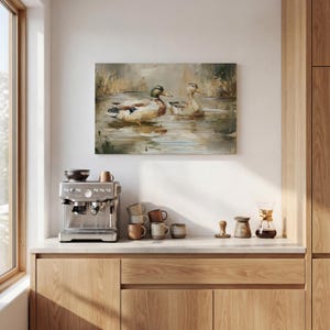 a kitchen counter with a coffee machine, coffee cups, and a painting of ducks swimming in a pond.