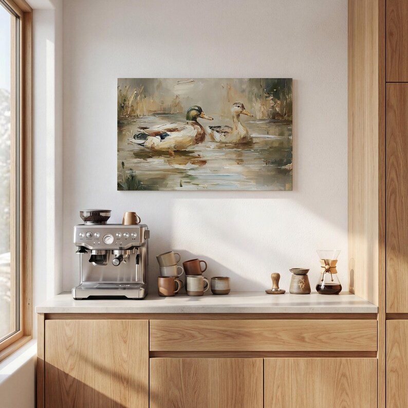 a kitchen counter with a coffee machine, coffee cups, and a painting of ducks swimming in a pond.