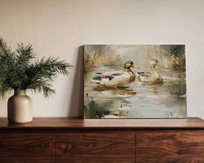 a painting of ducks swimming in a pond, displayed on a wooden shelf next to a vase with greenery.