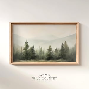 May include: A framed landscape print featuring a misty forest scene with tall evergreen trees and distant mountains. The artwork is in muted green and gray tones, set within a light wood frame. The text "WILD COUNTRY COLLECTIVE" is at the bottom.