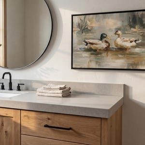 a bathroom scene with a round mirror, a wooden vanity, and a framed painting of ducks on the wall.