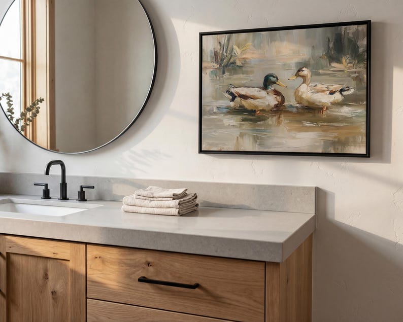a bathroom scene with a round mirror, a wooden vanity, and a framed painting of ducks on the wall.