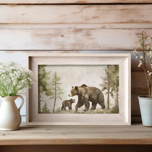 May include: A watercolor painting of a brown bear and a cub walking through a forest. The bears are walking on a path in the woods, surrounded by green trees and bushes.