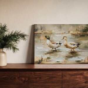 a wooden dresser with a painting of two ducks standing in a pond, and a vase of greenery on the left side of the dresser.