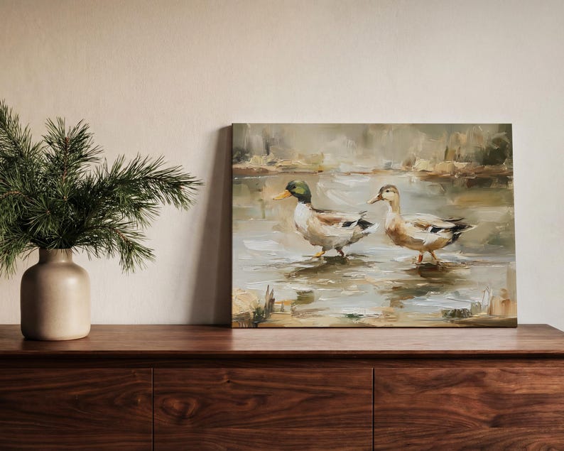 a wooden dresser with a painting of two ducks standing in a pond, and a vase of greenery on the left side of the dresser.