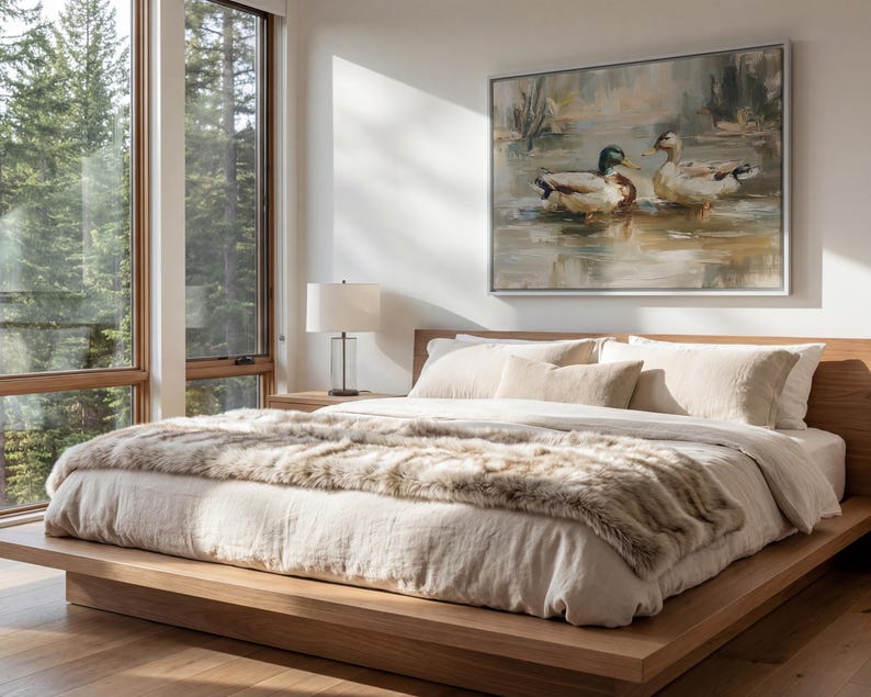 a serene bedroom scene with a large bed, a painting of ducks on the wall, and a window overlooking a wooded area.