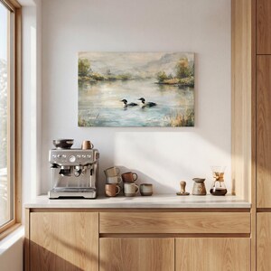 a kitchen counter with a coffee machine, coffee cups, and a painting of ducks in a lake.