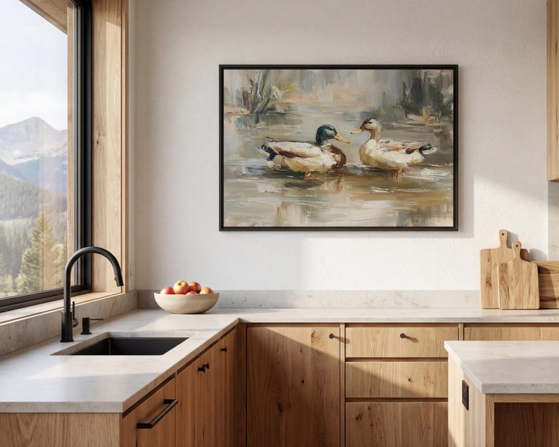a kitchen with a large painting of ducks swimming on the wall above a sink. The kitchen has wooden cabinets and a countertop, and there is a bowl of fruit on the counter.