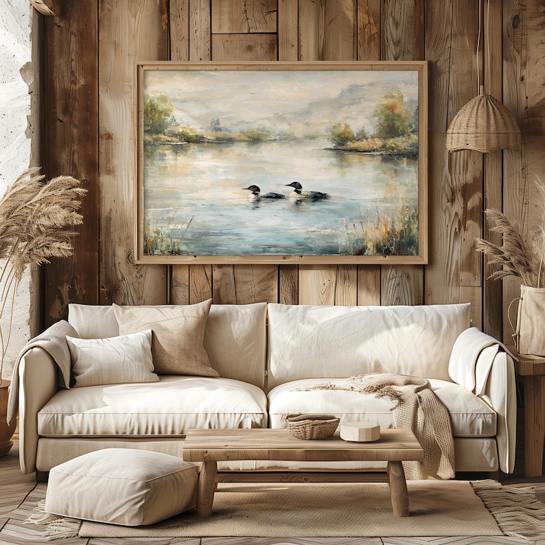 a cozy living room with a large painting of ducks swimming on a lake hanging on the wall above a beige sofa. The room has a rustic, cabin-like atmosphere with wooden walls and a wooden floor.