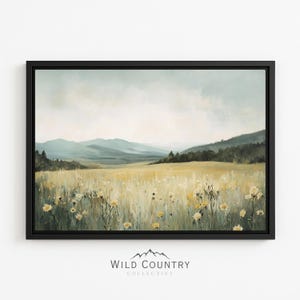 May include: A framed landscape painting featuring a field of yellow wildflowers in the foreground, a line of dark green trees in the mid-ground, and soft blue mountains under a cloudy sky in the distance. The text WILD COUNTRY COLLECTIVE is below.