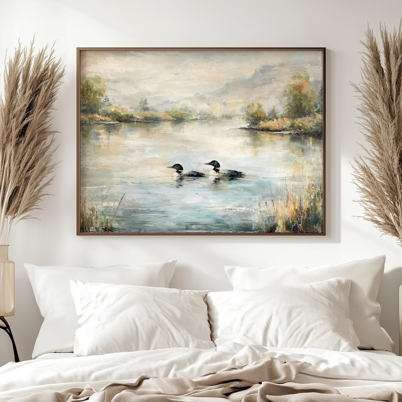 a large painting of two ducks swimming in a lake, hanging on a wall above a bed with white pillows.
