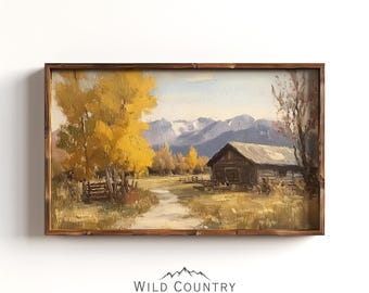 May include: A landscape oil painting in a dark wood frame depicting a rustic cabin in a field with golden autumn trees and distant snow-capped mountains under a pale sky. Below the frame, the text reads WILD COUNTRY COLLECTIVE.