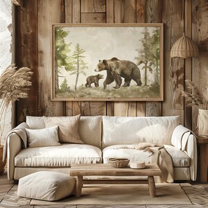 May include: A watercolor painting of a brown bear and her cub walking through a forest. The painting is framed in a light wood frame and is hanging on a wooden wall.